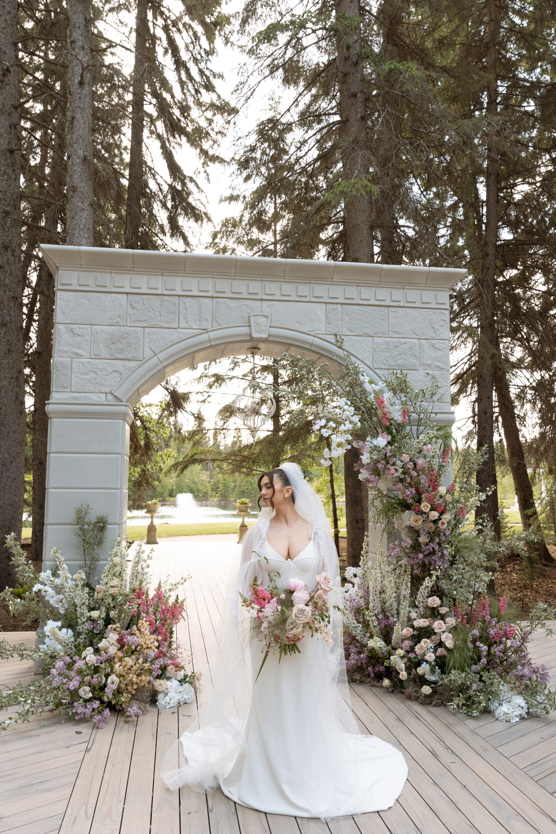 The bride in her stunning gown standing in front of the stone archway holding her bridal bouquet.