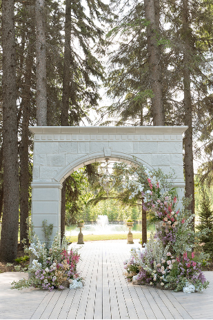 The 12ft stone archway at the outdoor ceremony site, adorned with flowers and with the pond and fountain in the background.