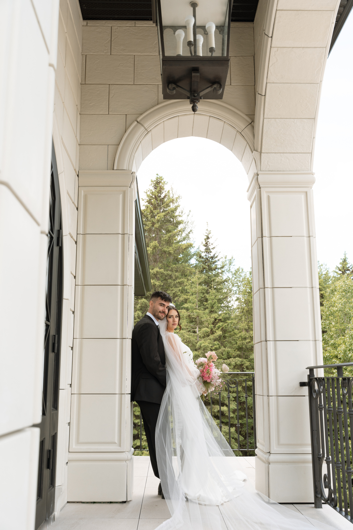 The bride leans against the groom under the arch on the balcony