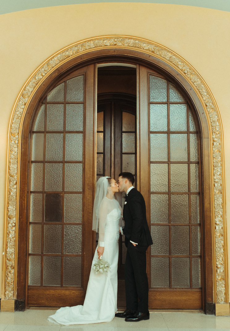 Tyller and Carter share a kiss in front of a beautiful glass panelled door with an ornate frame.