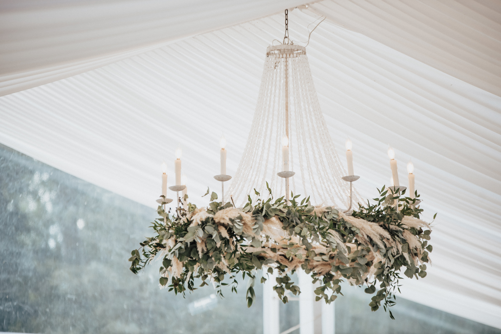 A detail shot of one of the chandeliers hanging from the draped ceiling with ruscus, pampas grass and eucalyptus.