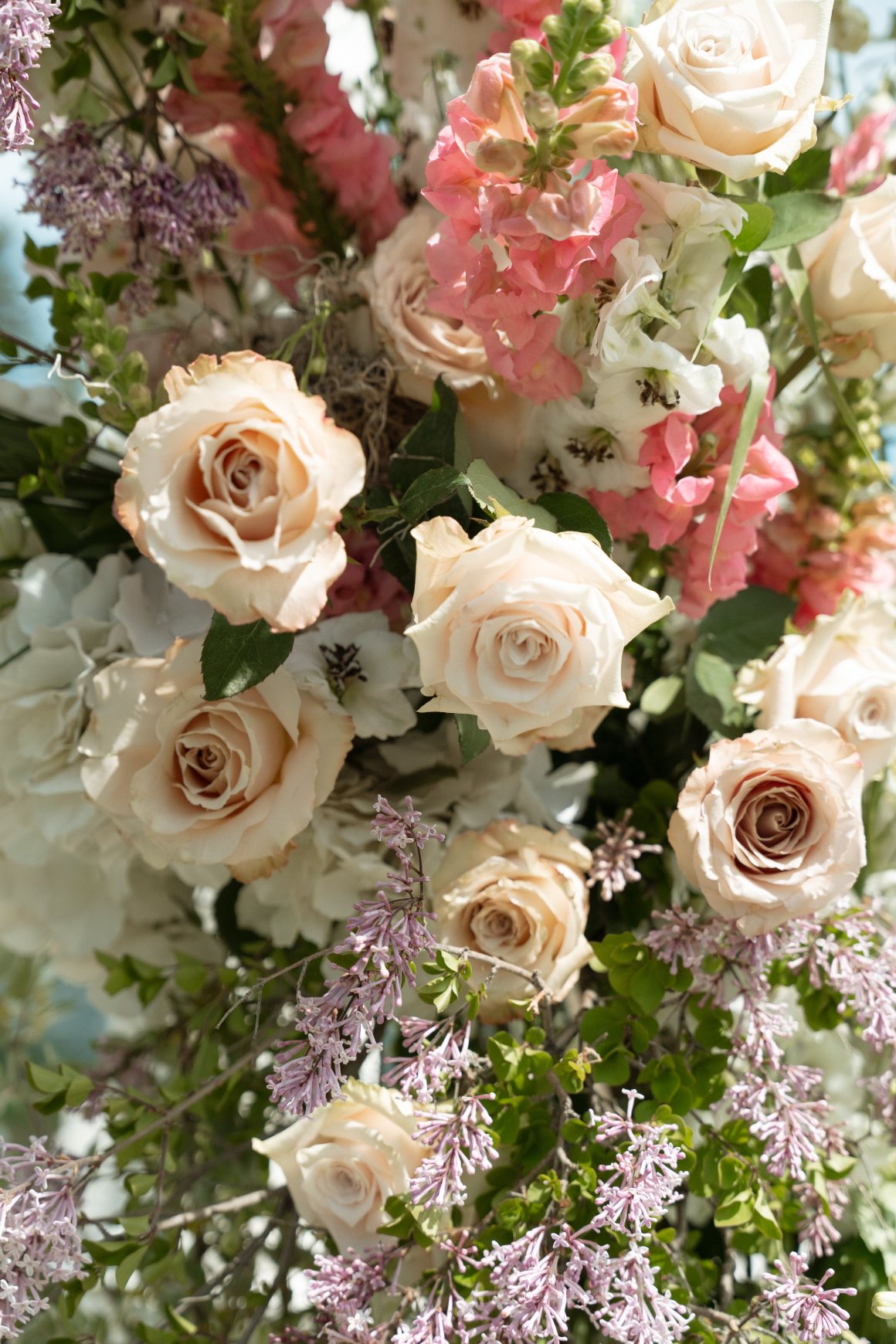 A close up of the floral arrangements with roses, delphinium, snapdragons, hydrangea and lilacs.