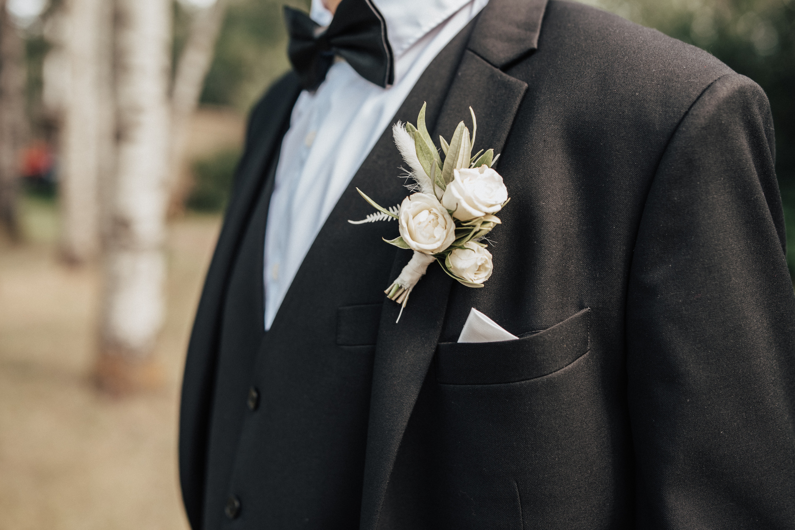Scott' sharp black tux, complete with a black bow tie. He wears a simple boutonniere of white spray roses, and olive branch.