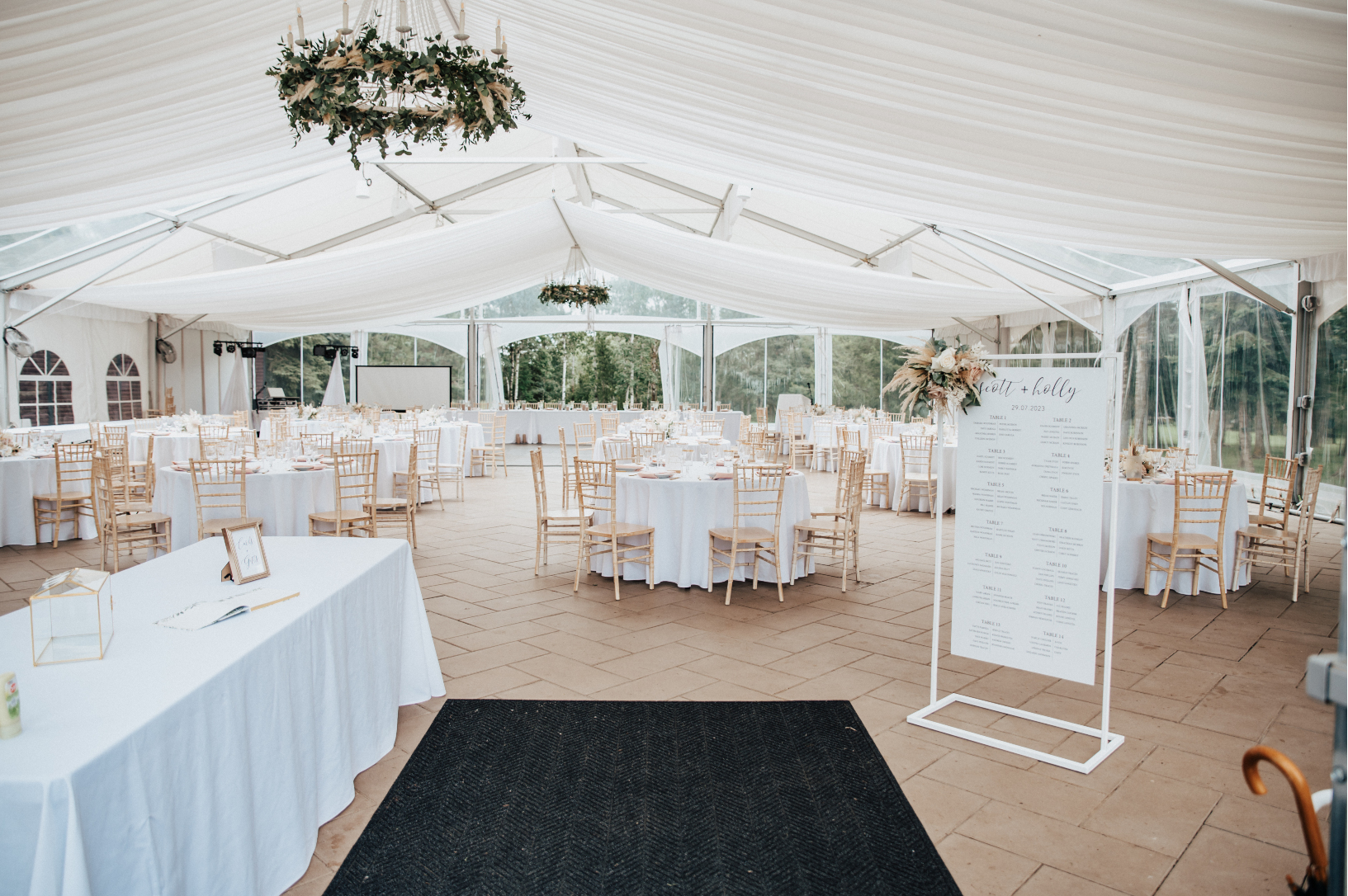 The overall reception set up inside the tent at Hilltop Wedding Center. A guestbook table to the left, seating chart to the right, greenery chandeliers hanging from the ceiling and the tables beautifully styled with centrepieces to match the rest of the flowers.