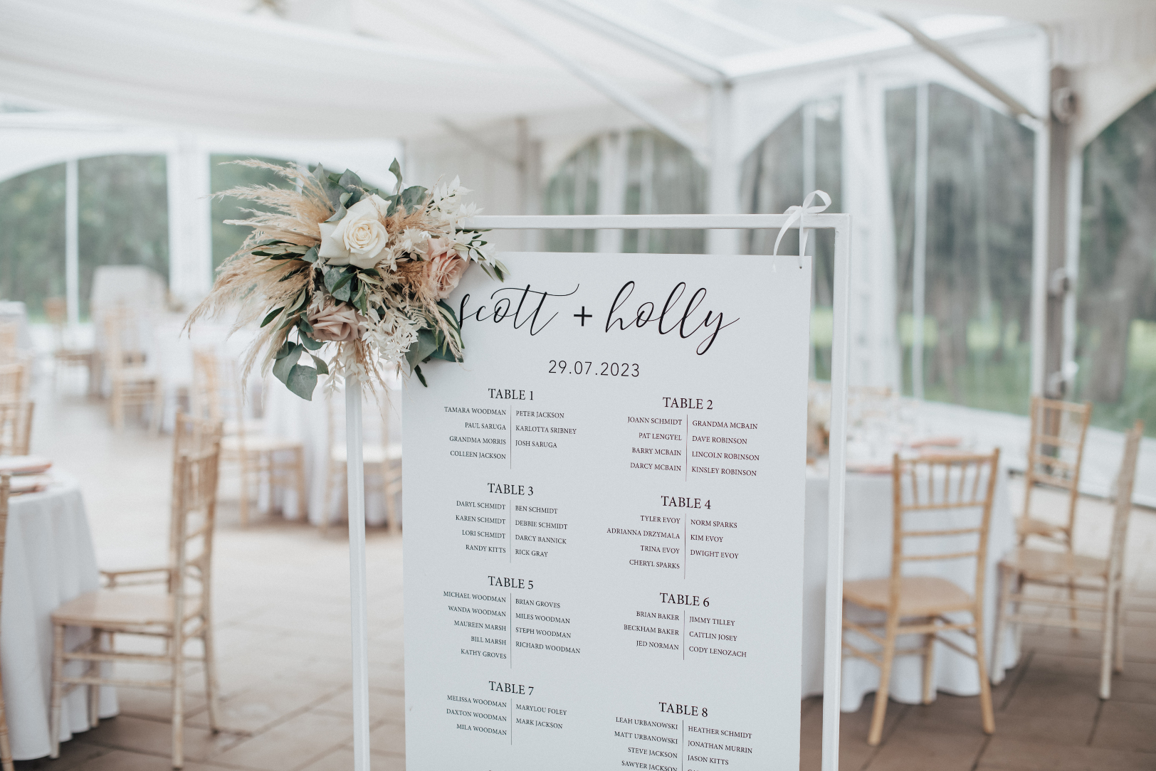 The seating chart with an arrangement of roses, pampas gras, eucalyptus, olive branch, bleached ruscus and smaller dried palm.