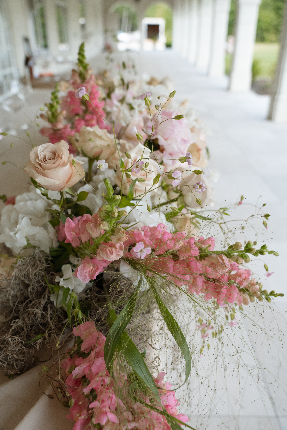 A close up of the low long arrangement across the sweetheart table with snapdragons, roses, hydrangea, peonies, decorative grasses, sweet peas, cherry blossoms, and delphinium.