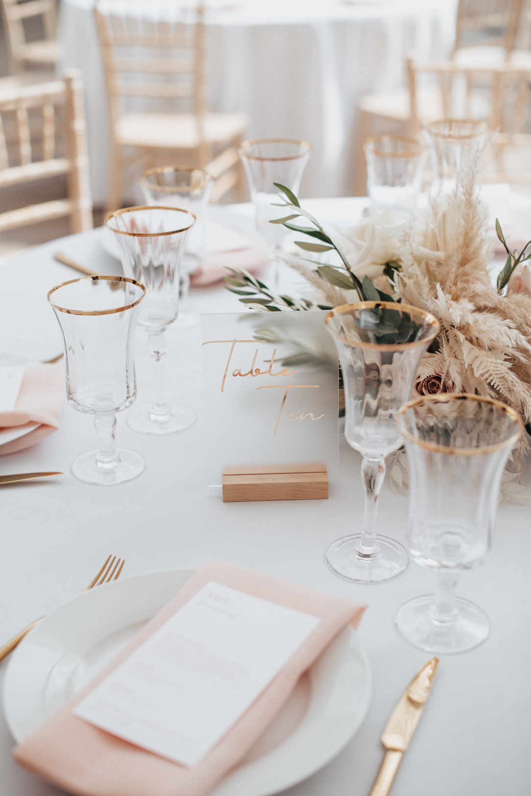 Gorgeous styled details of the guest tables, including beautiful frosted glass table numbers and centrepieces of roses, pampas grass, olive branch, eucalyptus, dried palm, bleached bracken fern and bleached ruscus.