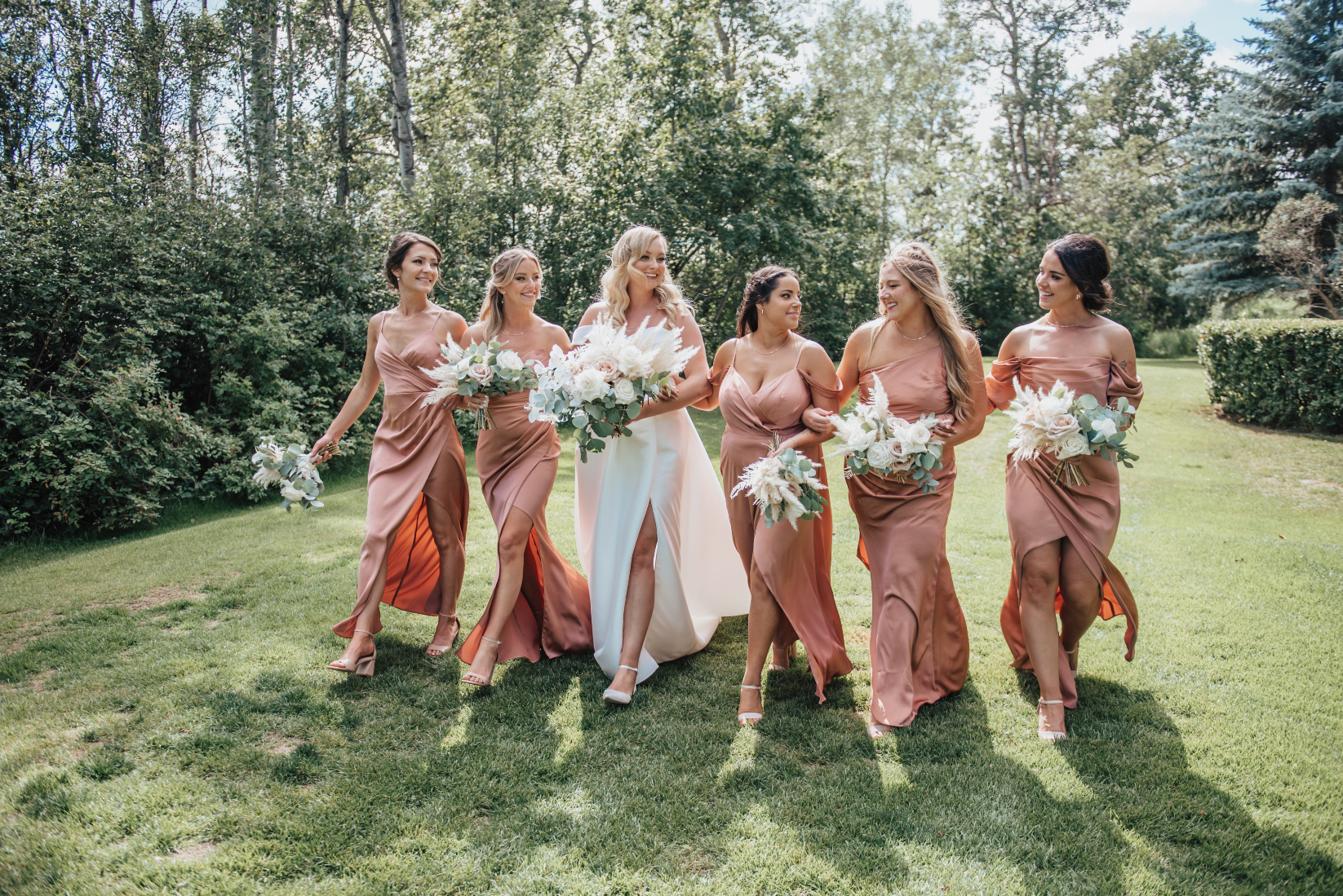 Holly and her bridesmaids have linked arms and are holding their bouquets as they walk together laughing and chatting.