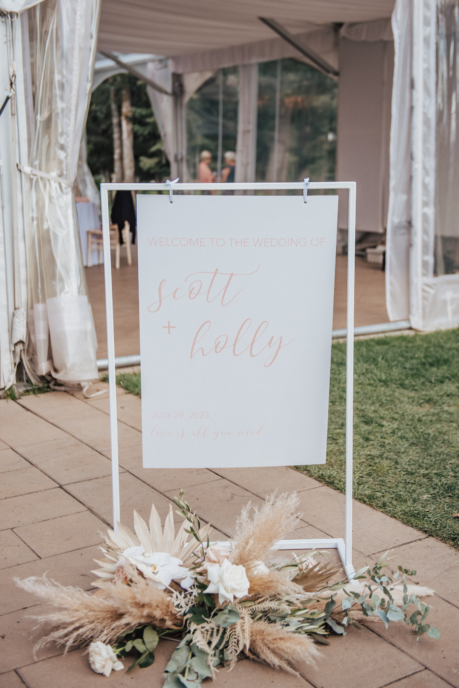 A welcome sign at the entrance of the reception at Hilltop, with a gorgeous arrangement of pampas grass, dried palms, bleached ruscus, roses, orchids, eucalyptus and olive branch.