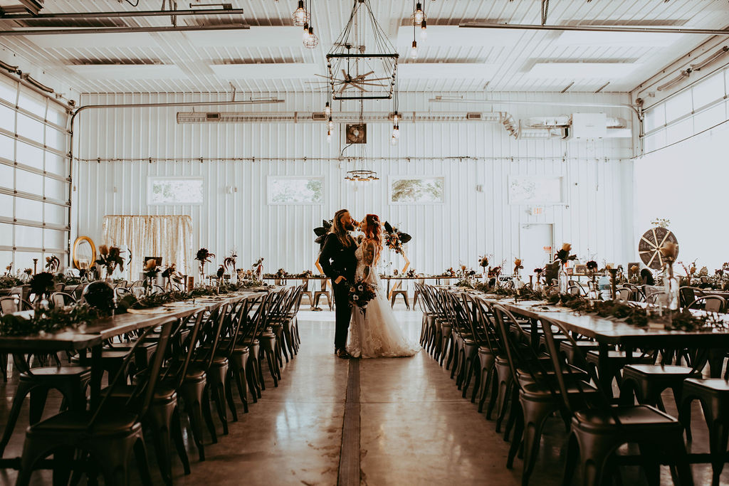 The cool, industrial inspired space of 52 North set up for their reception. Haley and Greg stand closely in between tables, facing each other.