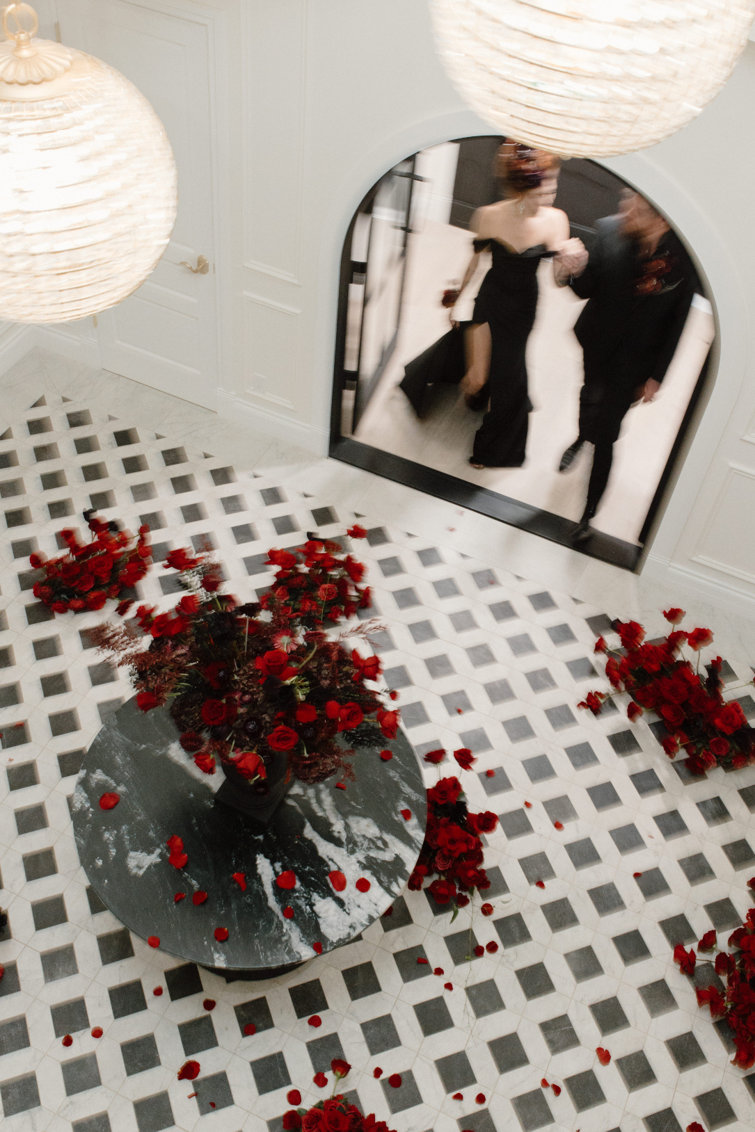 Dracula and his bride entering the foyer of Archway Manor, with a huge, stunning arrangement of red sits on the marbled round table.
