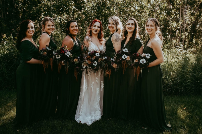 Haley and all of her beautiful bridesmaids standing close together, holding their bouquets and smiling.