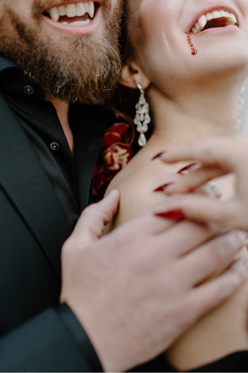 A close up of Dracula and his bride, laughing, showing off their fangs, and the red jewels at the corner of her mouth to appear like blood dripping from her mouth.