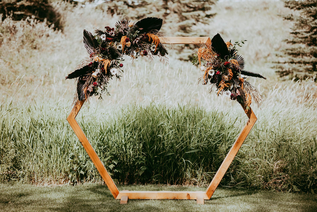 Beautiful wooden hexagonal shaped arch, adorned with flowers at the two upright corners.