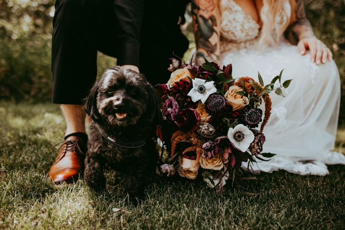 Haley and Greg squatting down next to their happy little fur baby, with Haley's gorgeous bouquet beside the dog.
