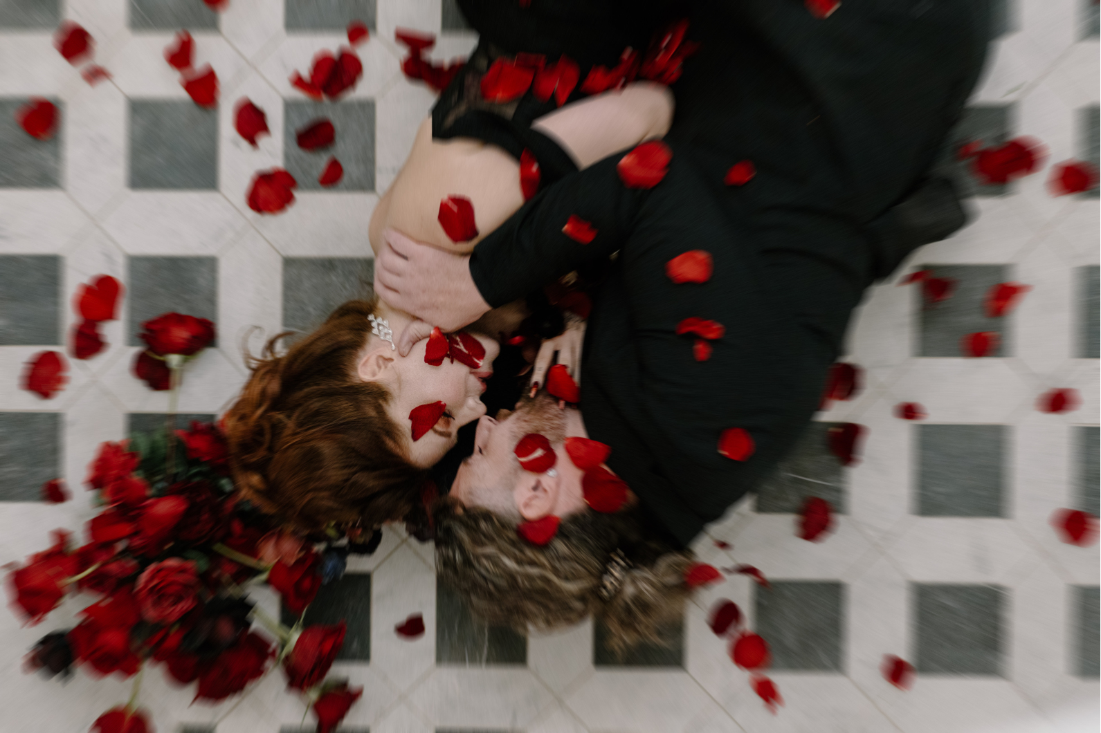 Dracula and his bride laying on the tiled floor, as red rose petals fall down on them.