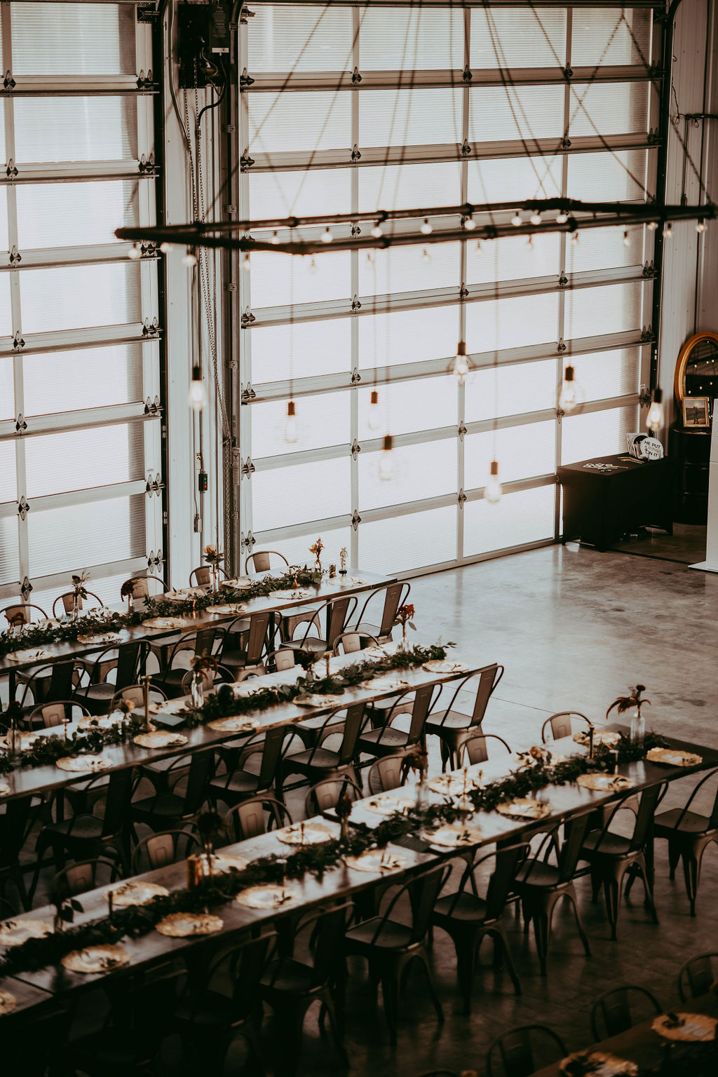 The reception set up in the cool, industrial space at 52 North with long, rectangular tables adorned with garlands and bud vases.