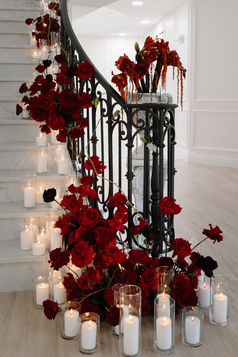 At the base of the stairs a big, striking arrangement in varying shades of red, surrounded by clusters of lit pillar candles at various heights.