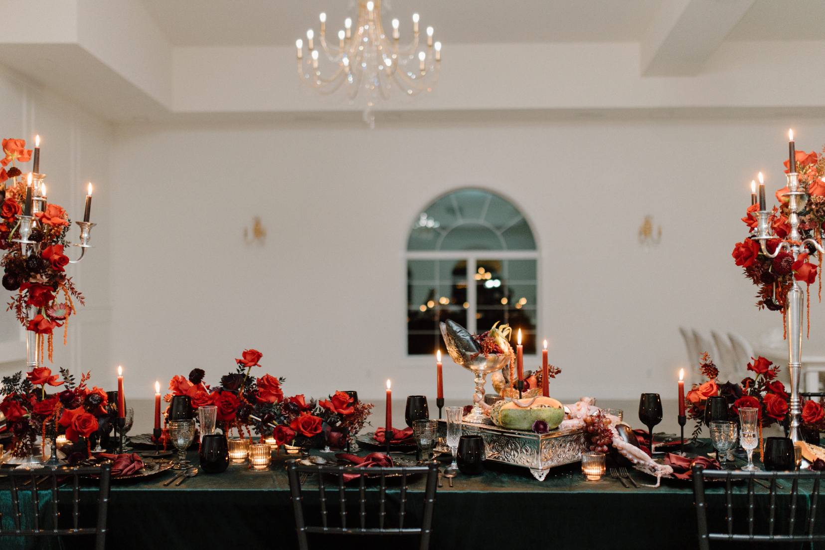 The length of the table, showing two big candleabras, oodles of red centrepieces at varying heights, with red tapered candles speckled down the table, with a serving tray covered with flowers, fruit and slimy seafood.