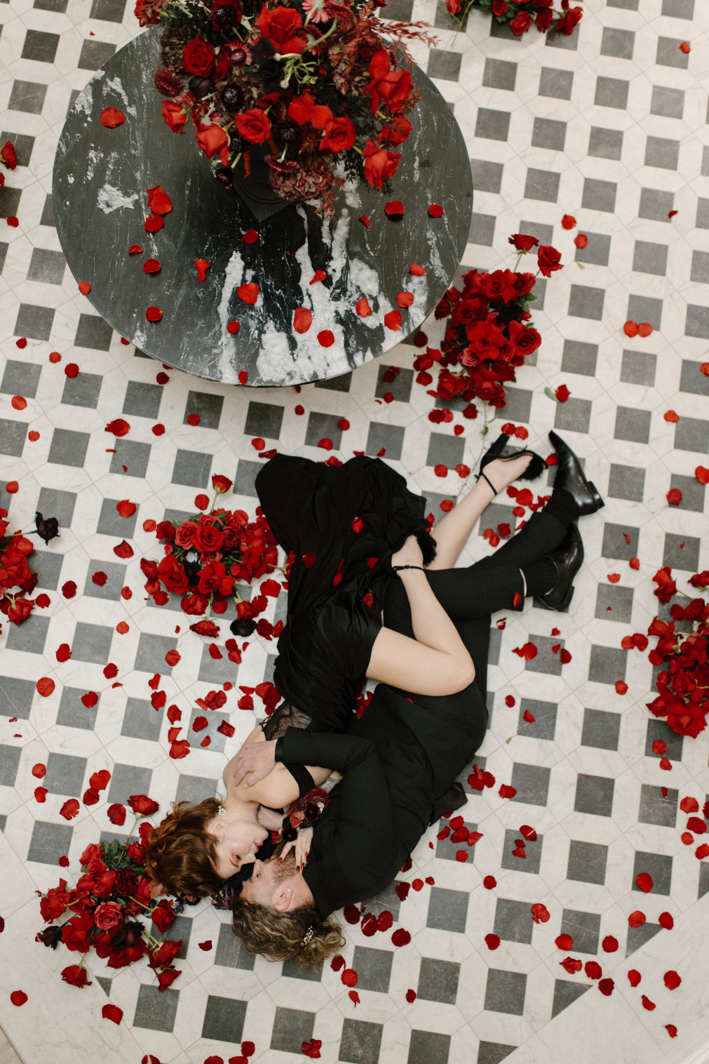 Dracula and his bride are entwined on the tiled floor, with red arrangements and red rose petals surrounding them.