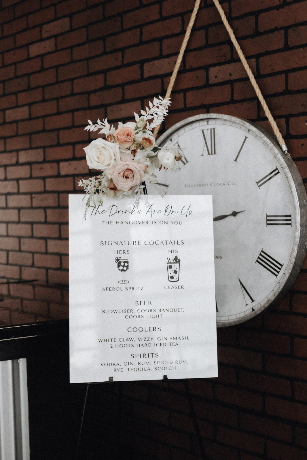 Another cute wedding sign for the bar, describing their signature cocktails, and available beverages. The sign has a little spray arrangement of astilbe, bleached ruscus, roses, lisianthus, roses and ranunculus.