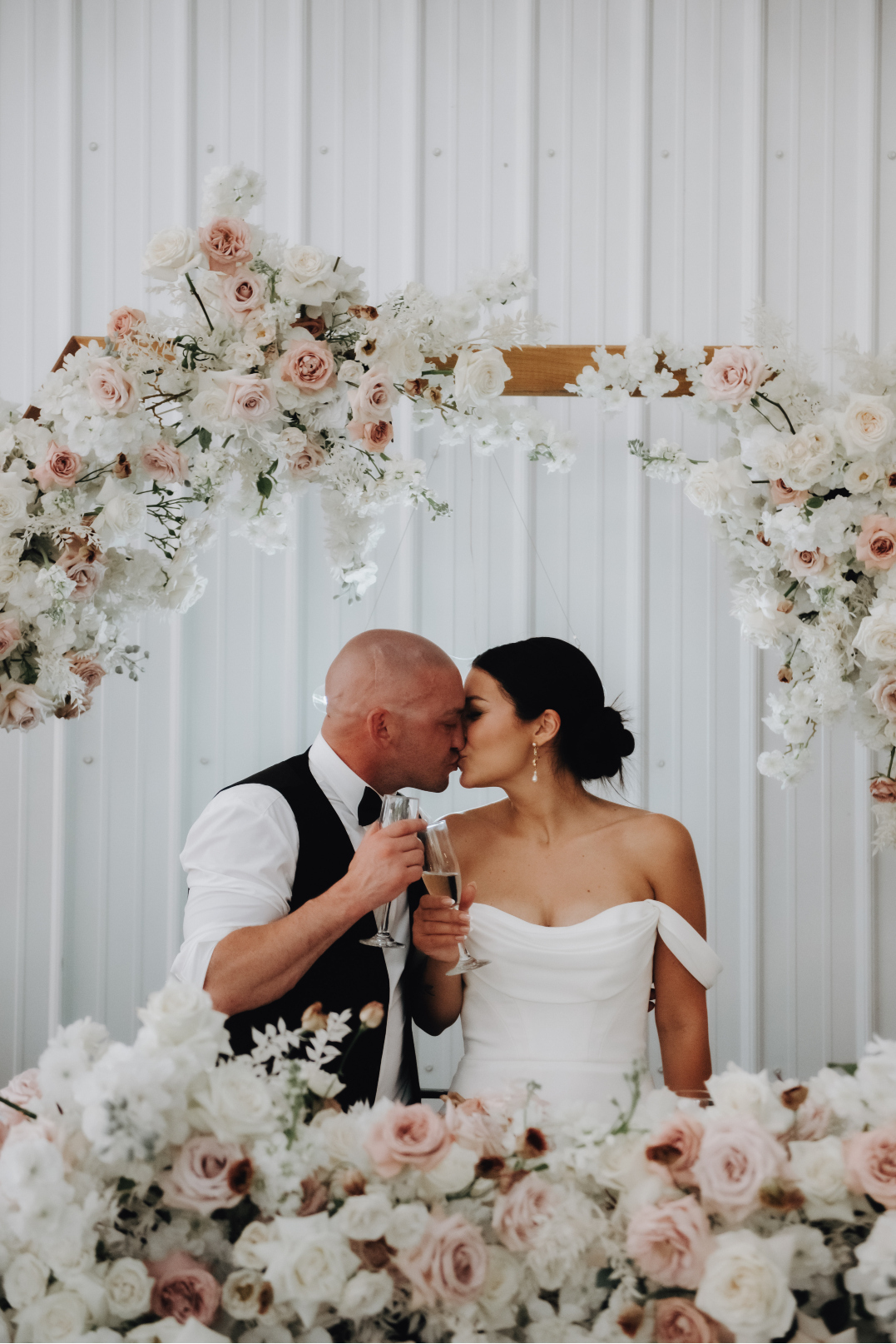 The beautiful couple sitting at the head table share a kiss.