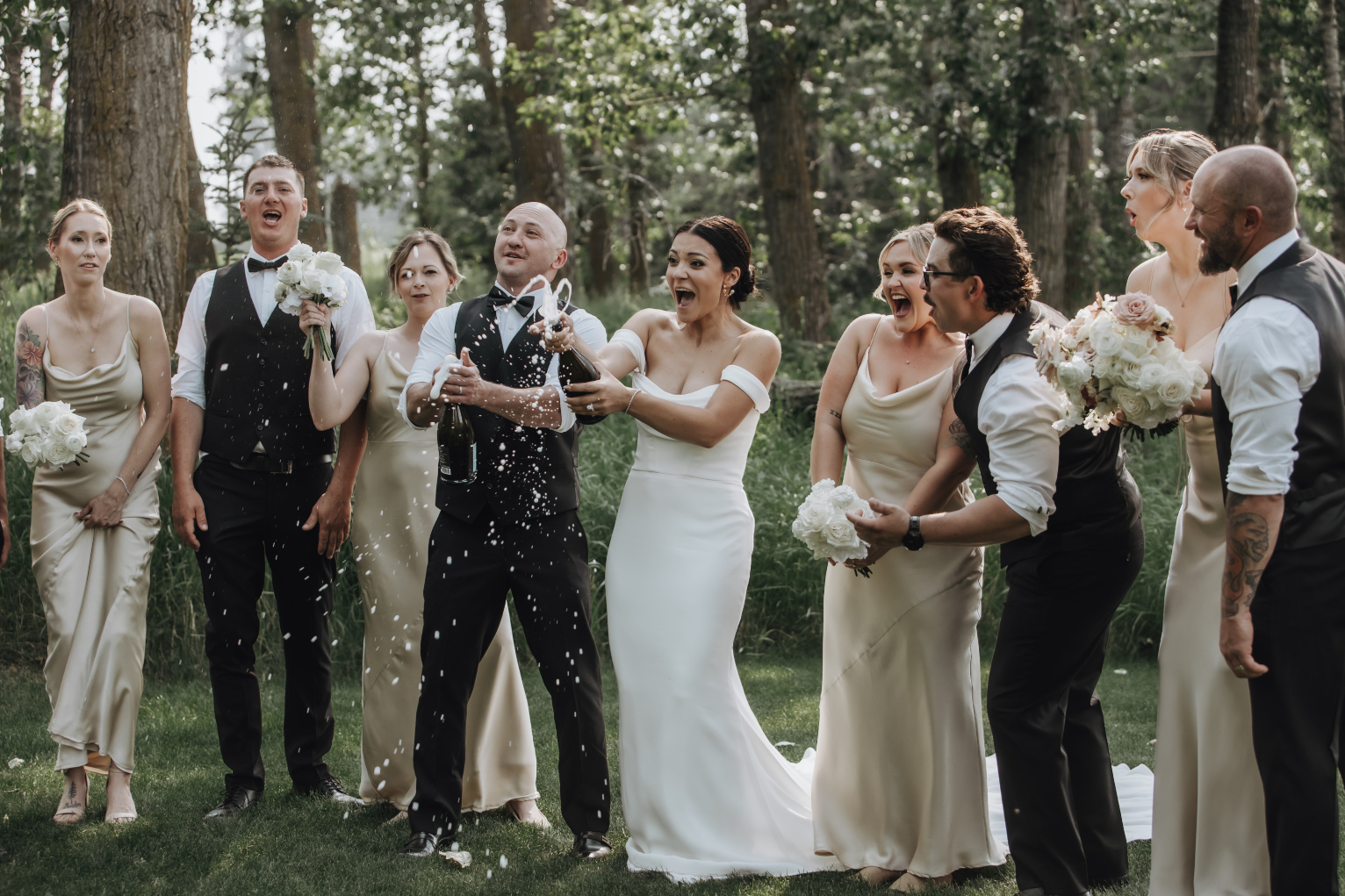 Kristen and Chris are with their wedding party, both holding a spraying champagne bottle in celebration