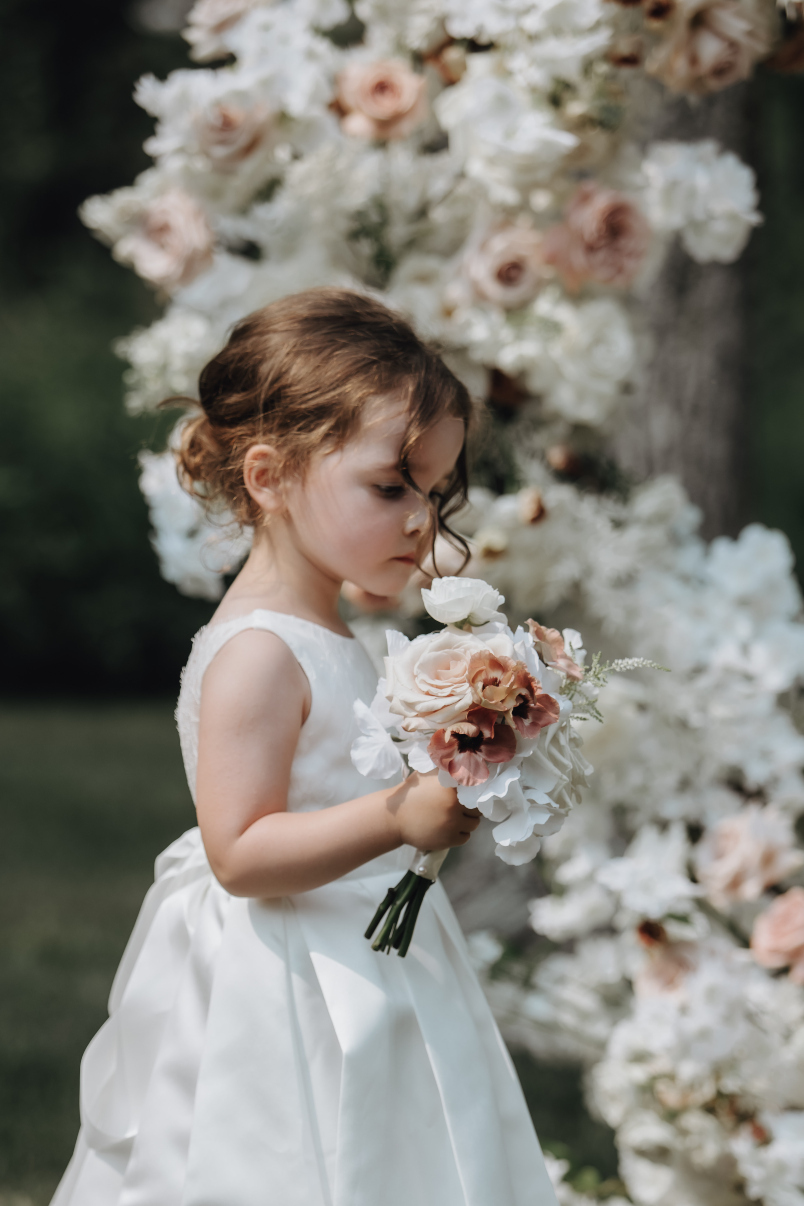 The couple's daughter as their flower girl, wearing a beautiful dress and looking adorable as she inspects her bouquet.