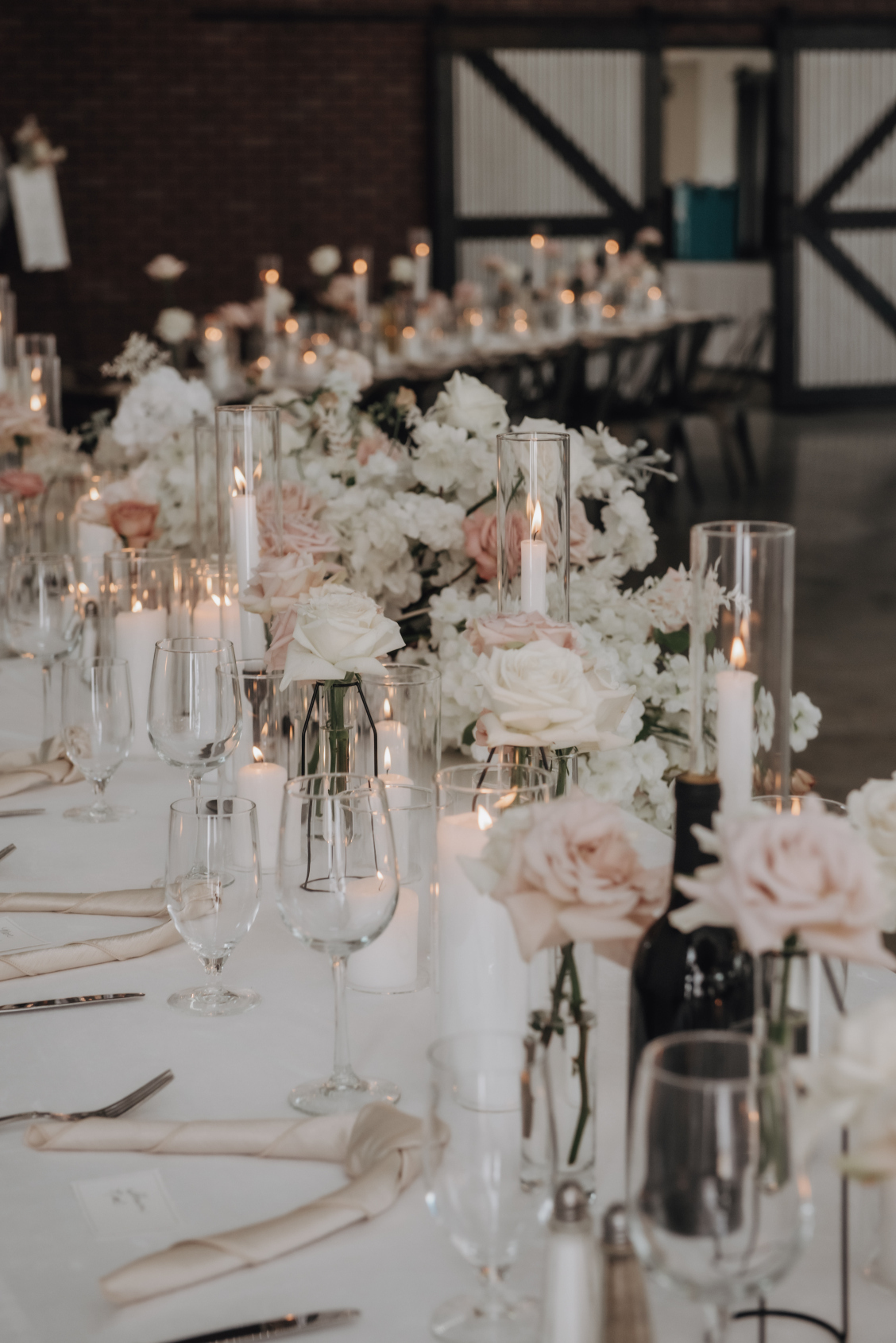 Long, rectangular guest tables are beautifully decorated with an assortment of candles, creating a lovely ambience, as well as rose bud vases for a very romantic feel.
