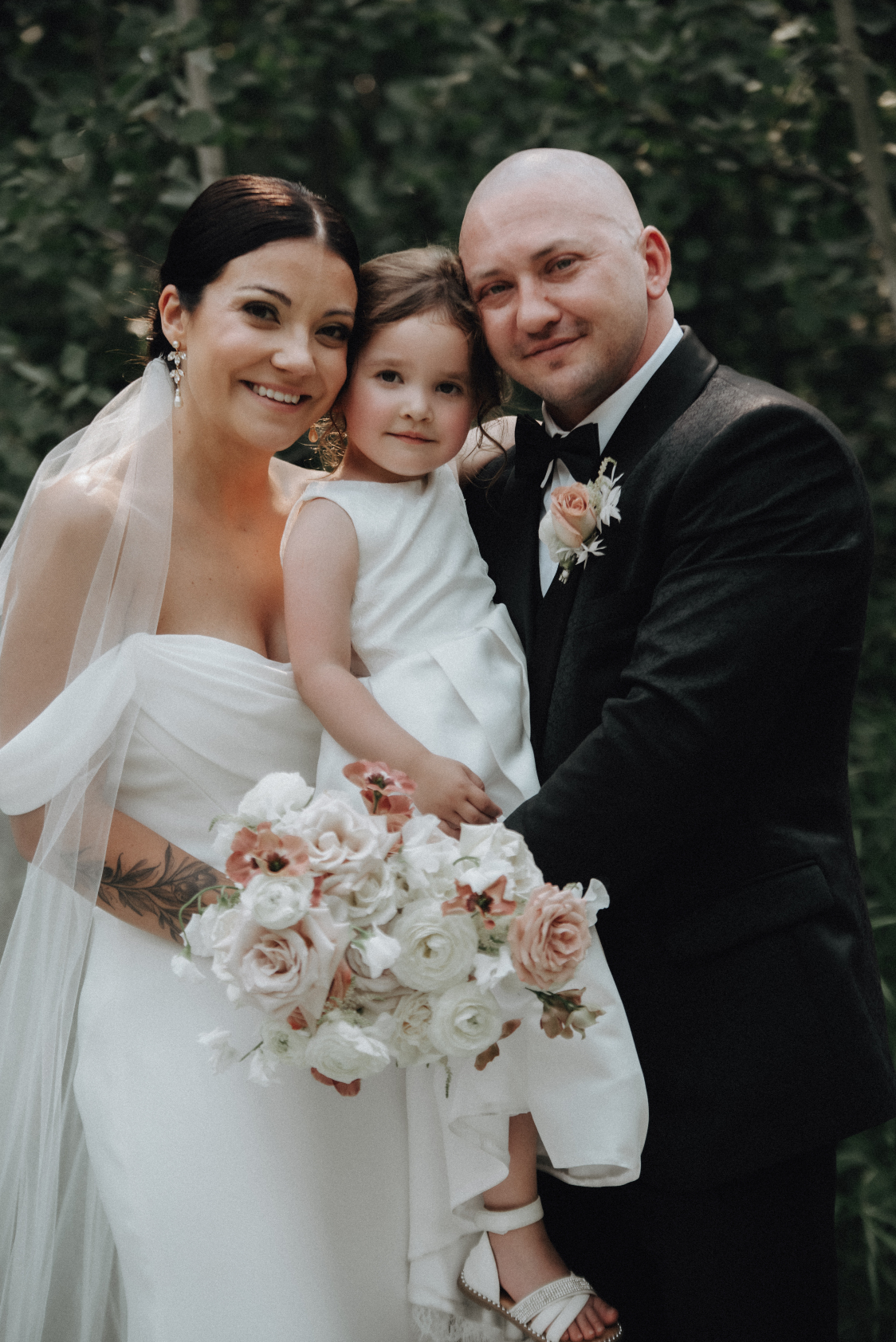 Kristen and Chris stand close together holding their daughter between them, all looking happy.