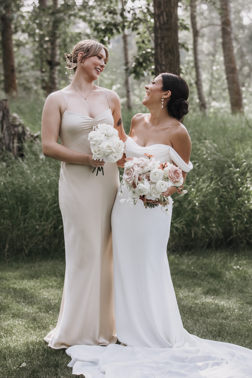 Kristen standing next to her charming bridesmaid, they are both looking to each other and laughing happily.