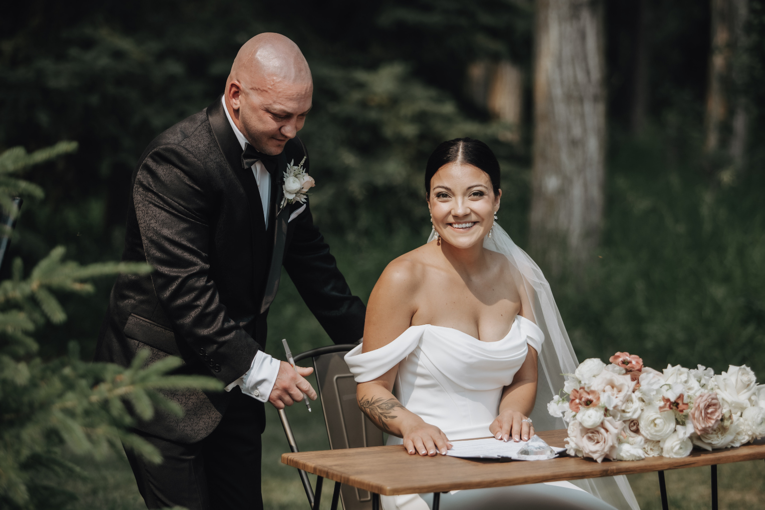 Kristin at the signing table, smiling from ear to ear as her husband helps her with her chair.
