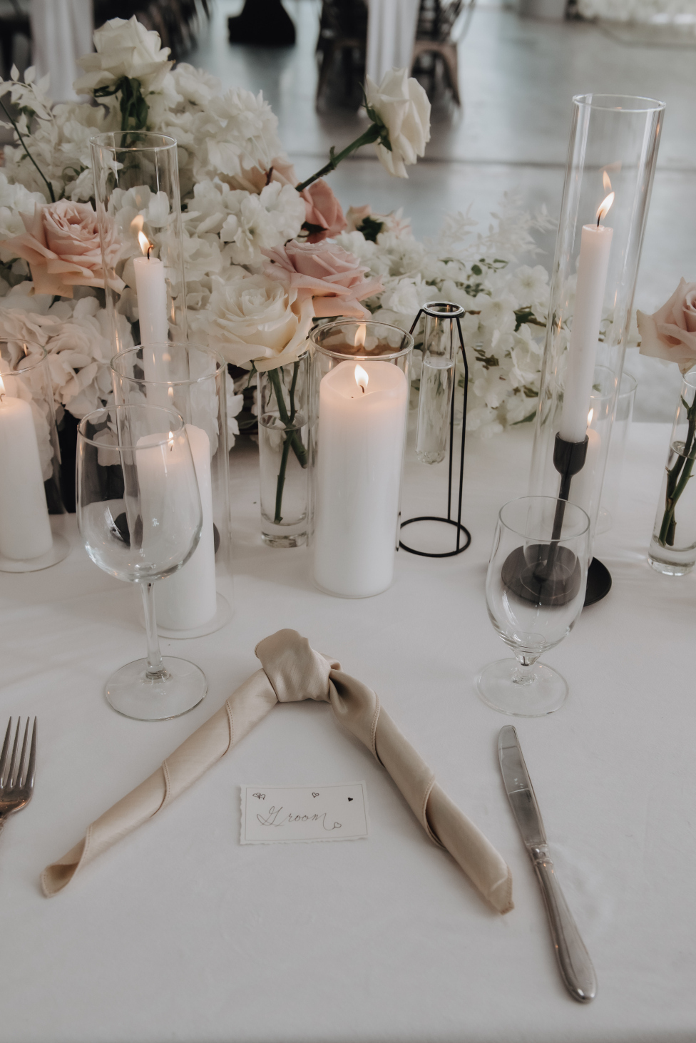 A place setting at the head table showcasing beautiful arrangement displayed on the table along with candles and a delicate champagne napkin tied napkin.