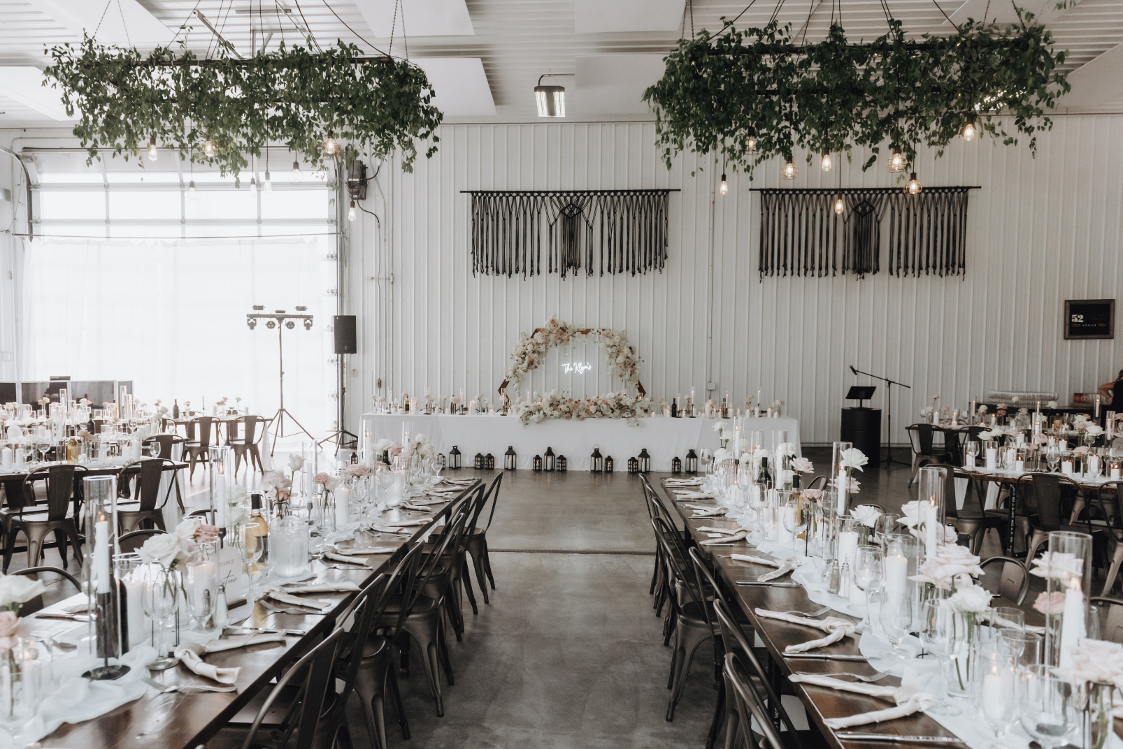 The set up of the reception space at 52 North, showing the greenery chandeliers, the stunning head table, and long rectangular tables for the guests.