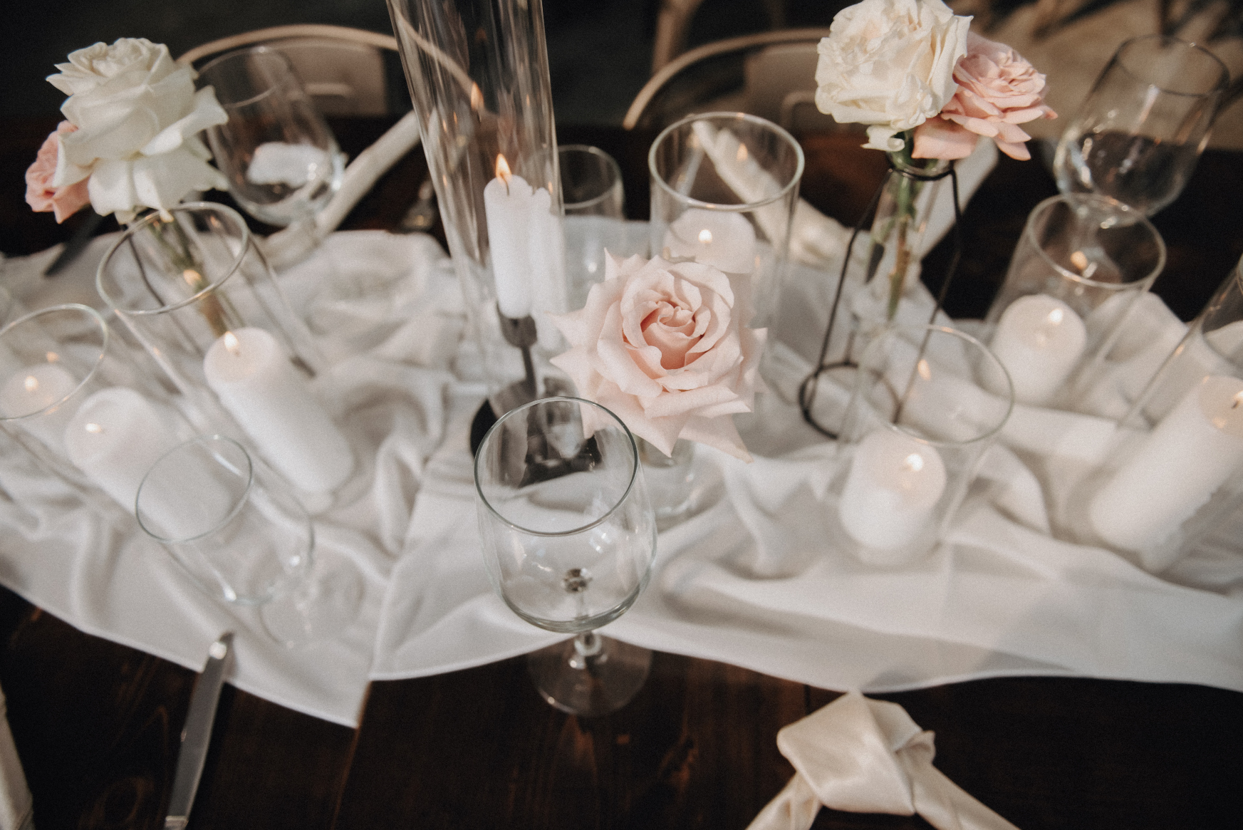 Romantic table centrepieces consisting of rose budvases tucked between groupings of candles white candles.