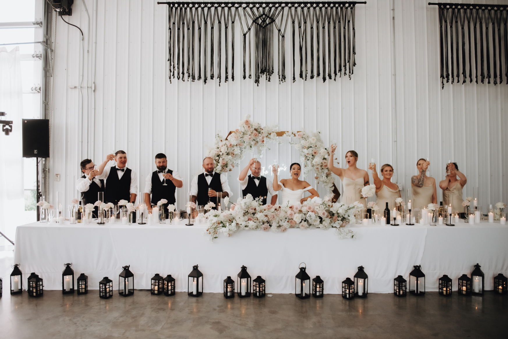 The wedding party all at the head table, standing up and raising their drinks in the air, toasting after a speech.