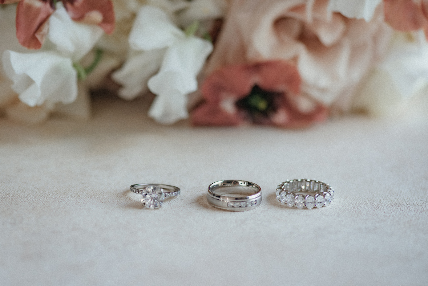Kristin's engagement ring, Chris' wedding band and Kristens wedding band, lined up in front of her bridal bouquet.