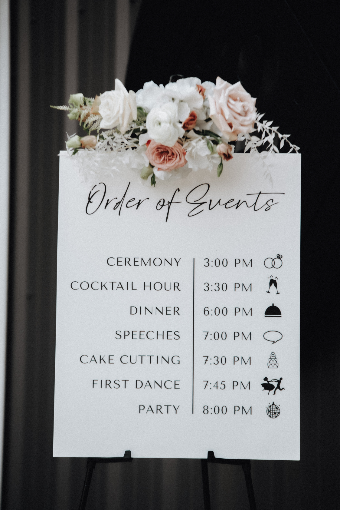 A wedding sign indicating the timeline for the evening is decorated with a mini arrangement in white and blush!