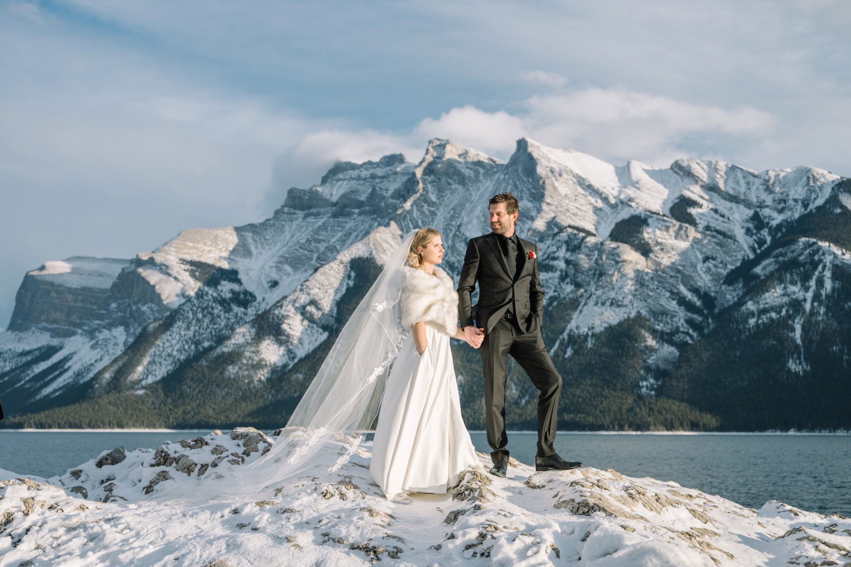 C+A Mountaintop A dramatic capture of Courtney and Adam stranding with a majestic mountain behind them. They are holding hands and Courtney's long veil drapes behind her.