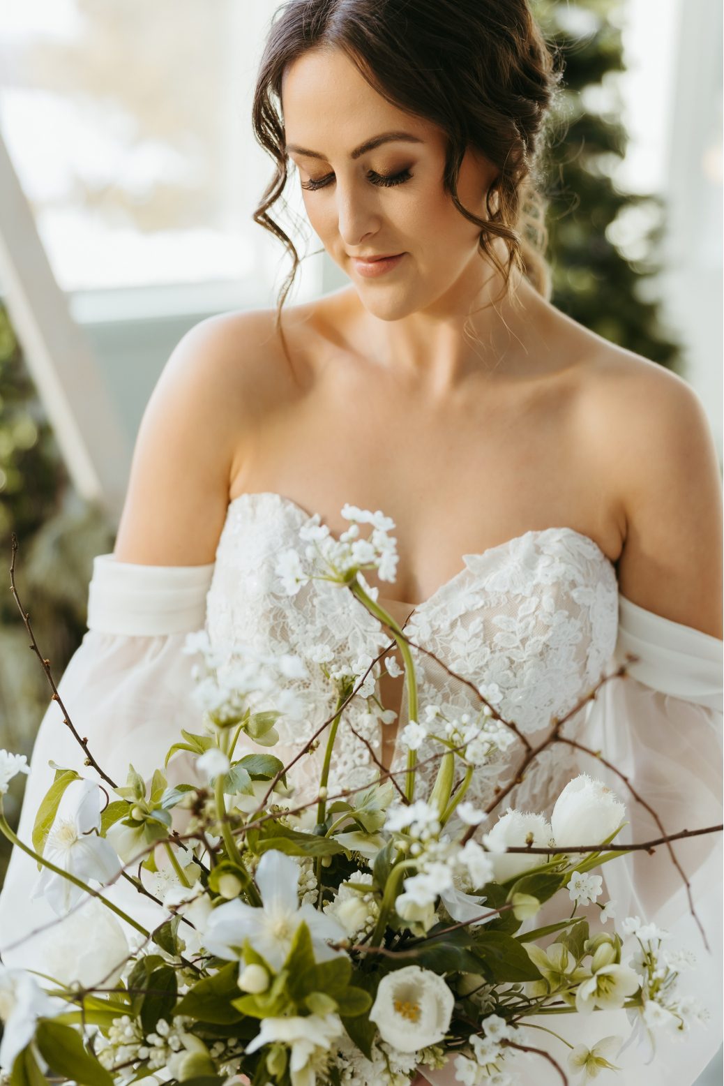 Our model bride in her stunning gown holding a white winter bouquet of hellebores, tulips, clematis, allium and lilac branches.