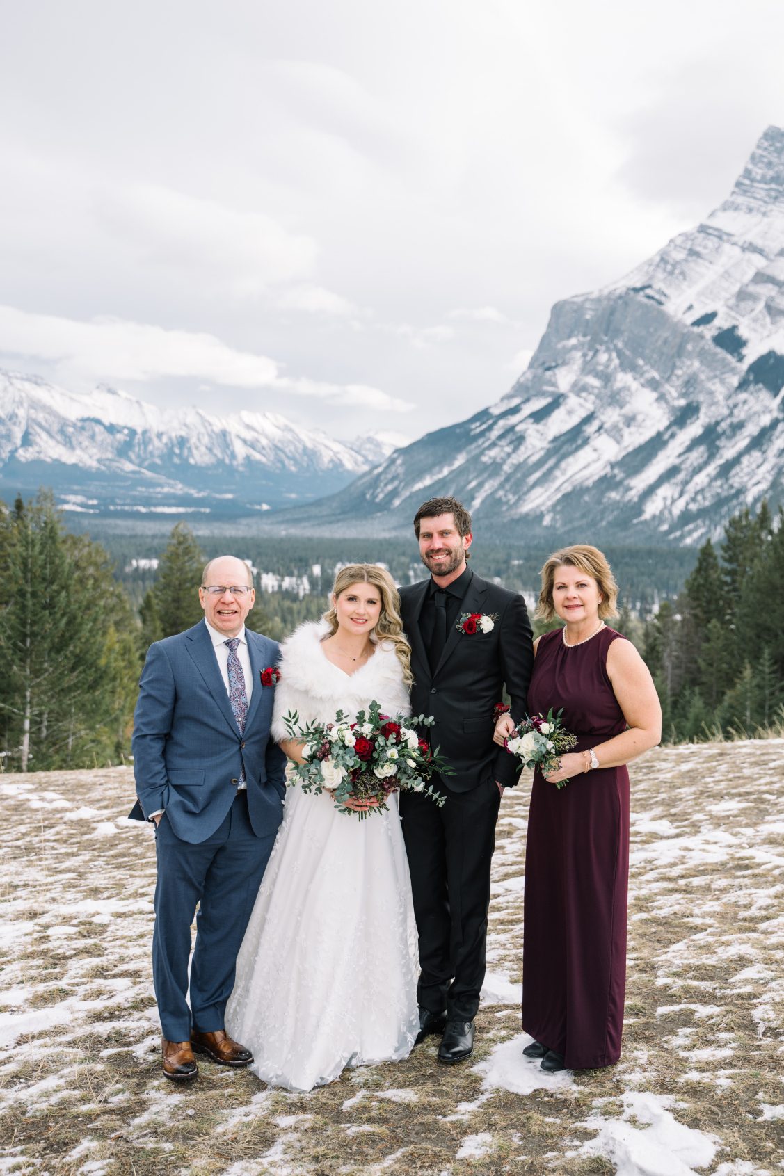 Calyx Couple + Parents Courtney and Adam stand with her parents with rocky mountains behind them.