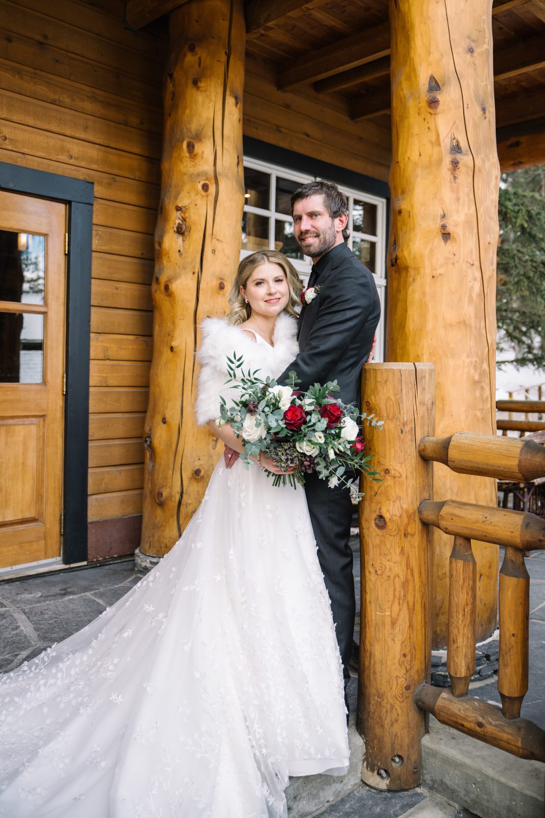 Calyx Couple at Lodge Courtney and Adam embrace in front of the Buffalo Mountain Lodge, and she is holding her stunning burgundy and ivory bouquet.