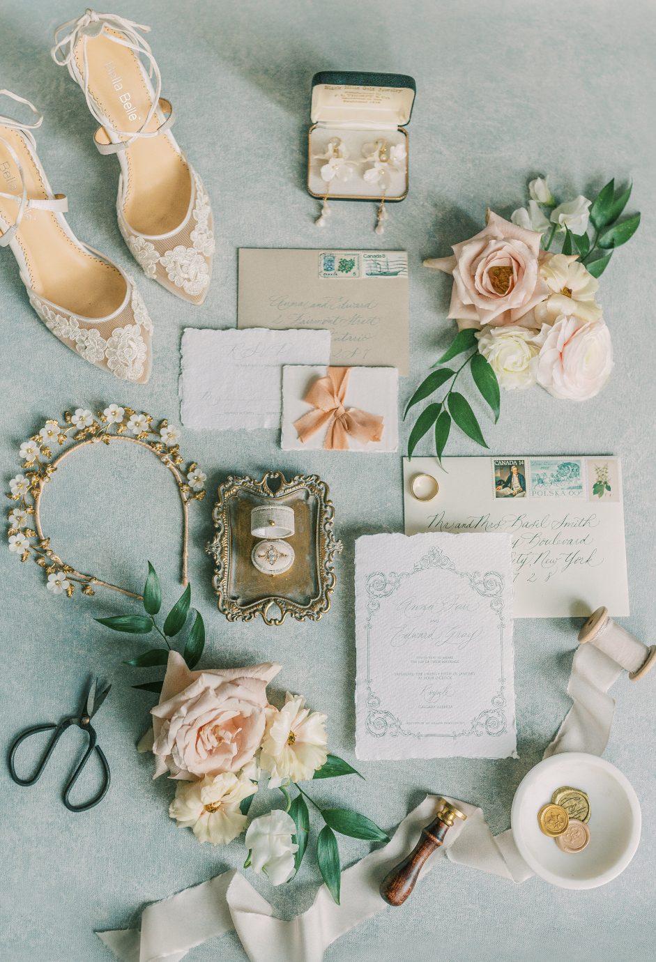 A flat lay image of beautifully coordinated wedding details including shoes, rings, headpiece, invitation an flowers.