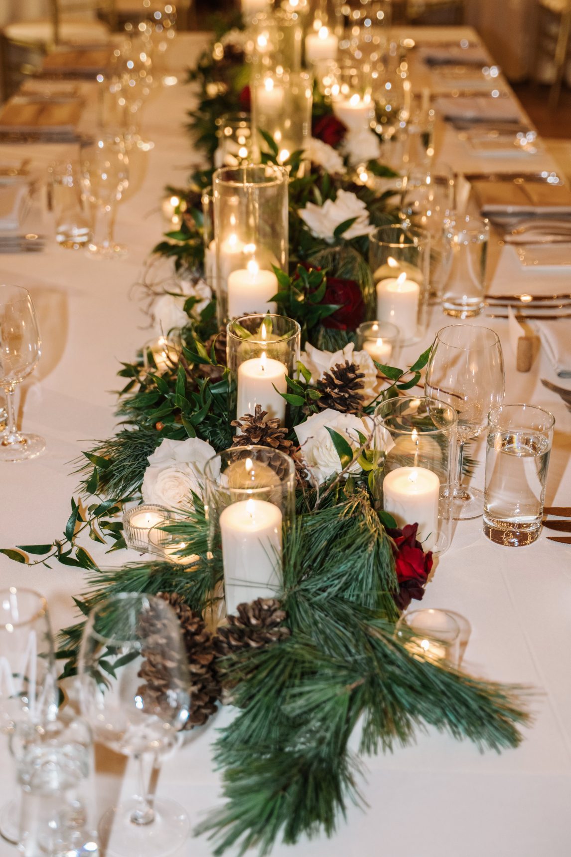 Head Table Decor Close up of the gorgeous head table floral runner, with winter greens, roses, pinecones and candles.