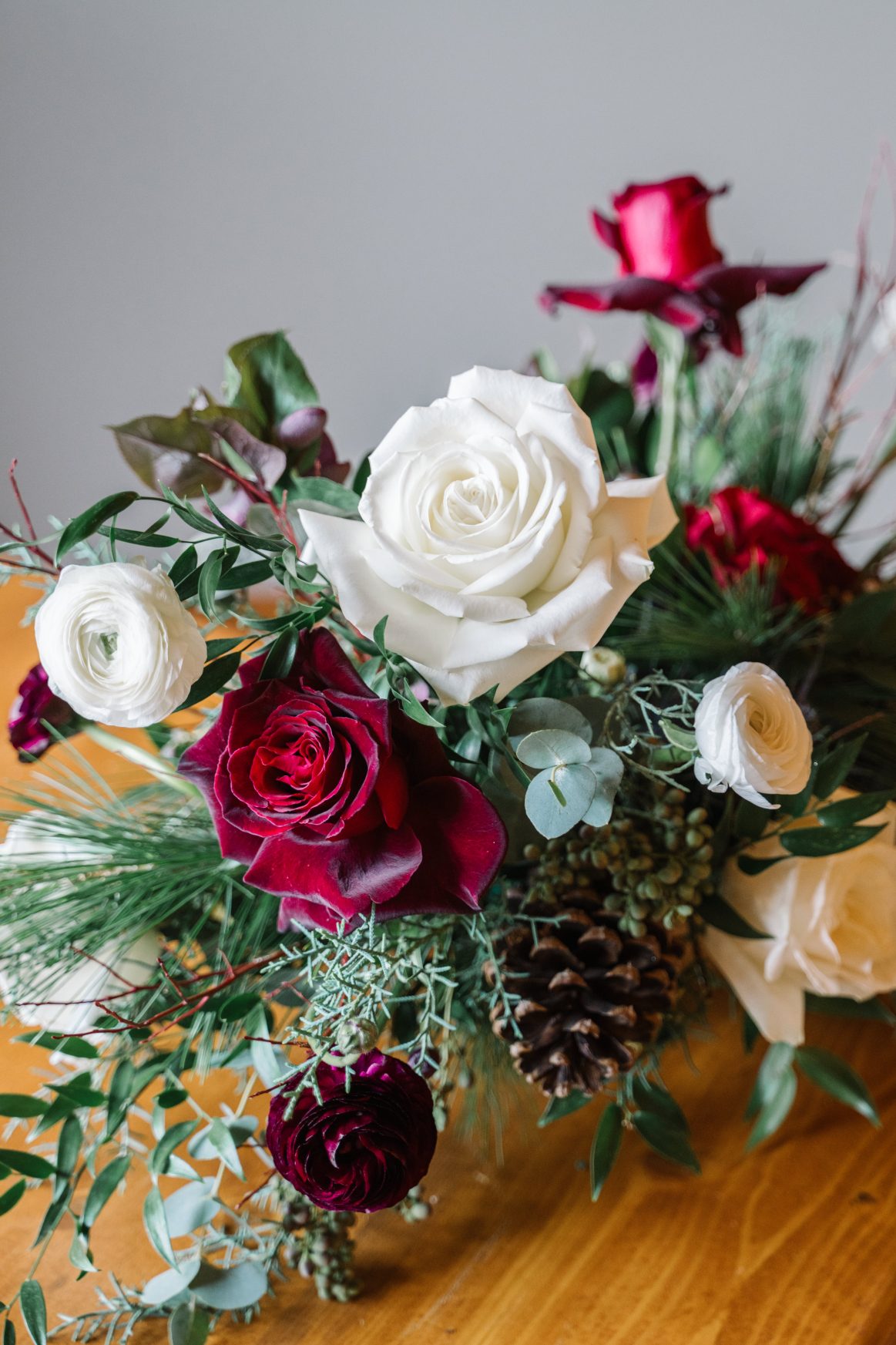 Romantic Centrepiece A close up of a stunning centrepiece with burgundy and ivory roses, ranunculus, eryngium, privet berries, hellebores, lush winter greens, eucalyptus and Italian ruscus in a gold compote container.