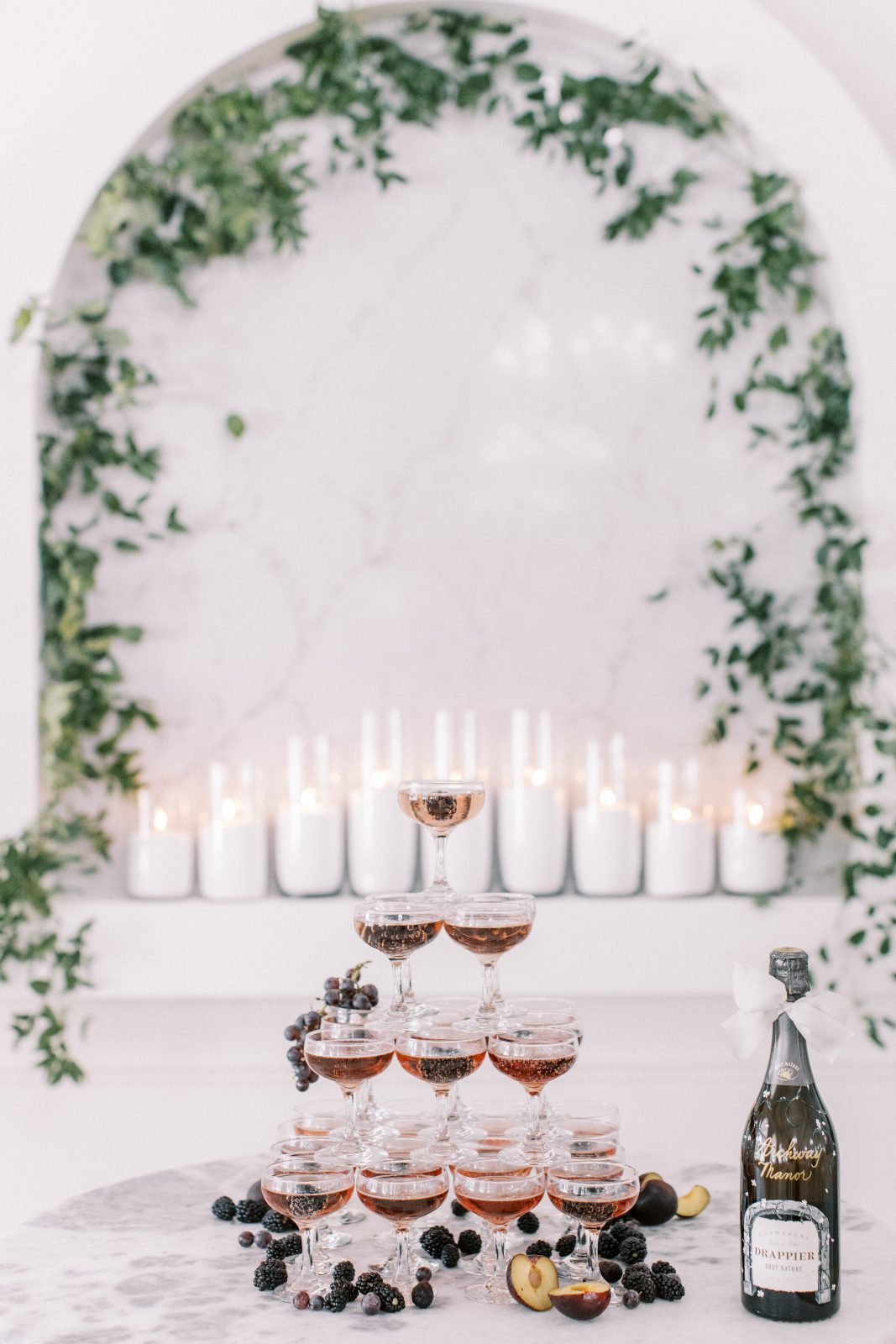 A tower of champagne with a romantic display of glowe candles in behind and the arch highlighted by lush greens.