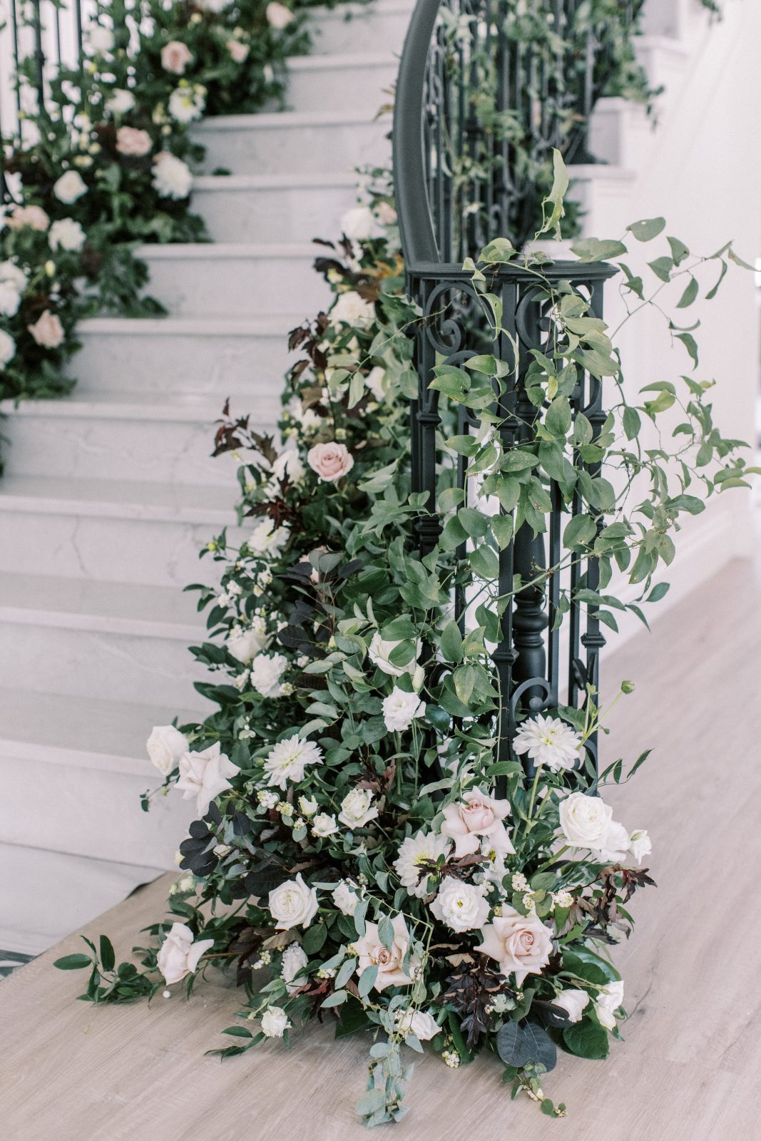 Lush greenery winding its way up the banisters of the dramatic staircase at Archway Manor, and peppered with creamy white blooms.