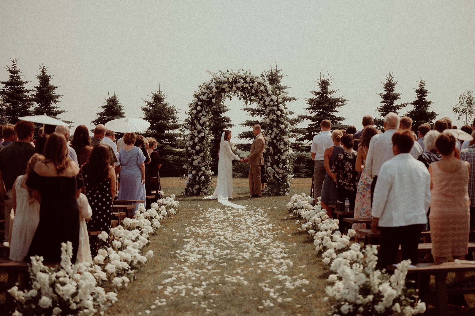 Looking down the aisle scattered in rose petals and lined with roses, the grand, romantic arch frames the stunning couple beautifully for the ceremony.