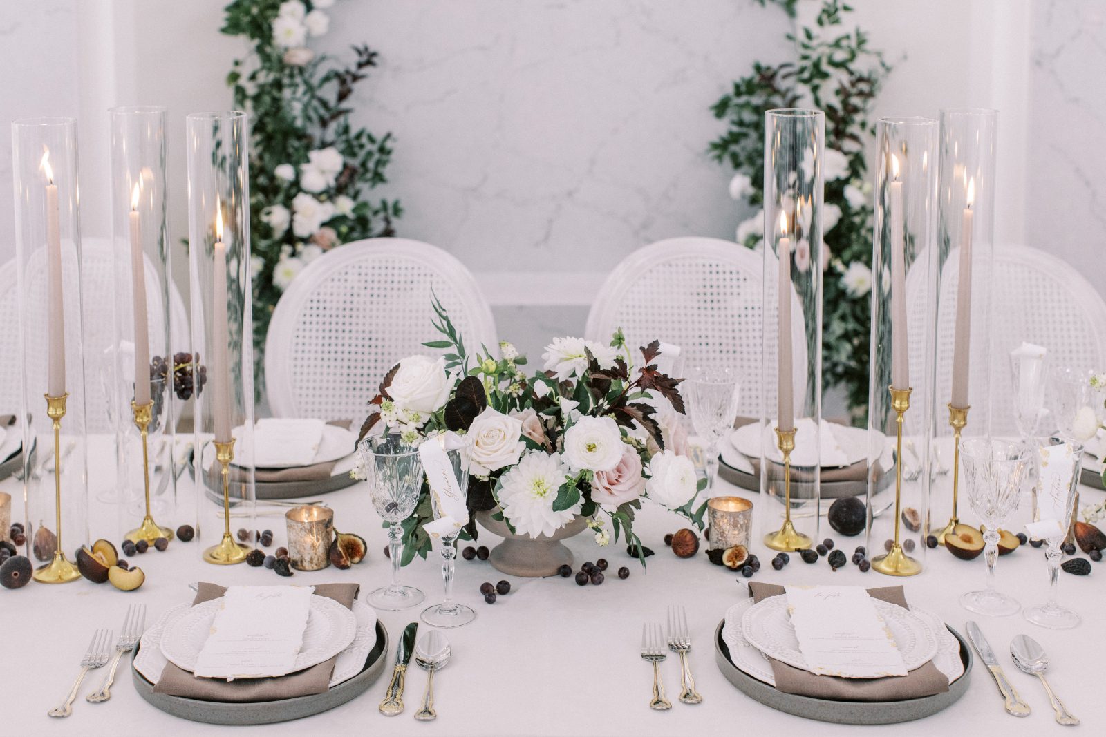A magnificent tablescape set up featuring creamy white blooms accented by rich burgundy tones, taupe and golden accents and luxurious place settings.