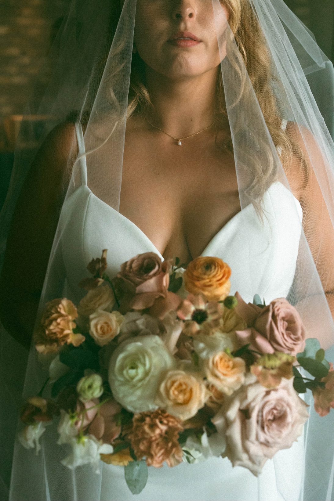 Shot of the bridal bouquet in blushes, ivory and peach tones featuring roses, ranunculus, spray roses, lisianthus, carnations and gunni eucalyptus.